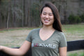 Front  View - Women's tan breeches with full seat in red and fox print pattern. Model stands in front of wooden fence wearing signature V-Neck womens riding t-shirt in gray with the breeches.